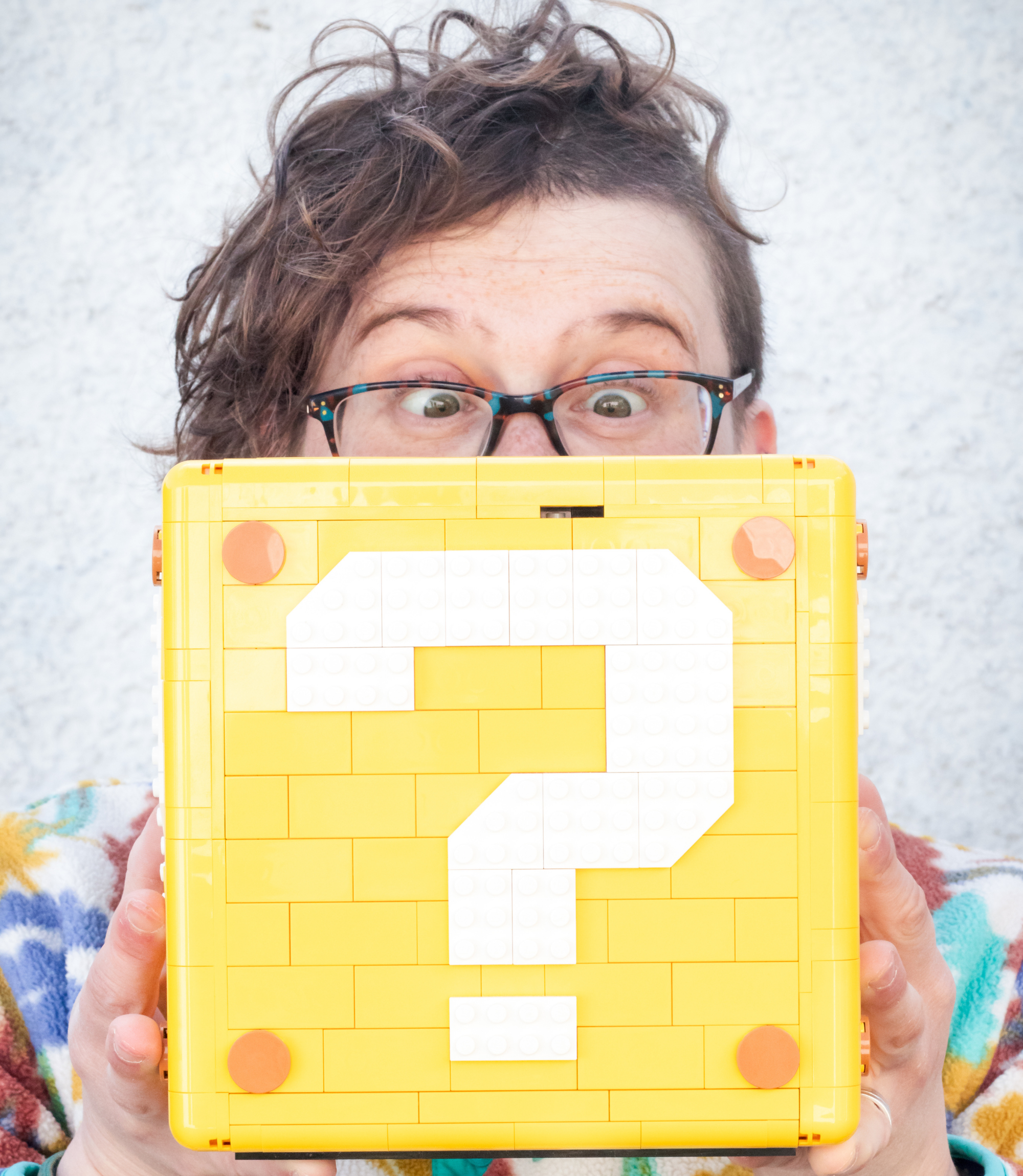A photo of Rebs in a colourful fleece, looking at a Lego question block. 